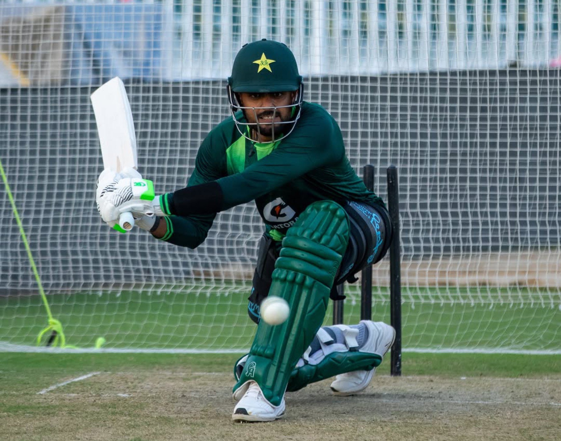 Cricket player in green Pakistan kit batting in a practice net, ball in mid‑air