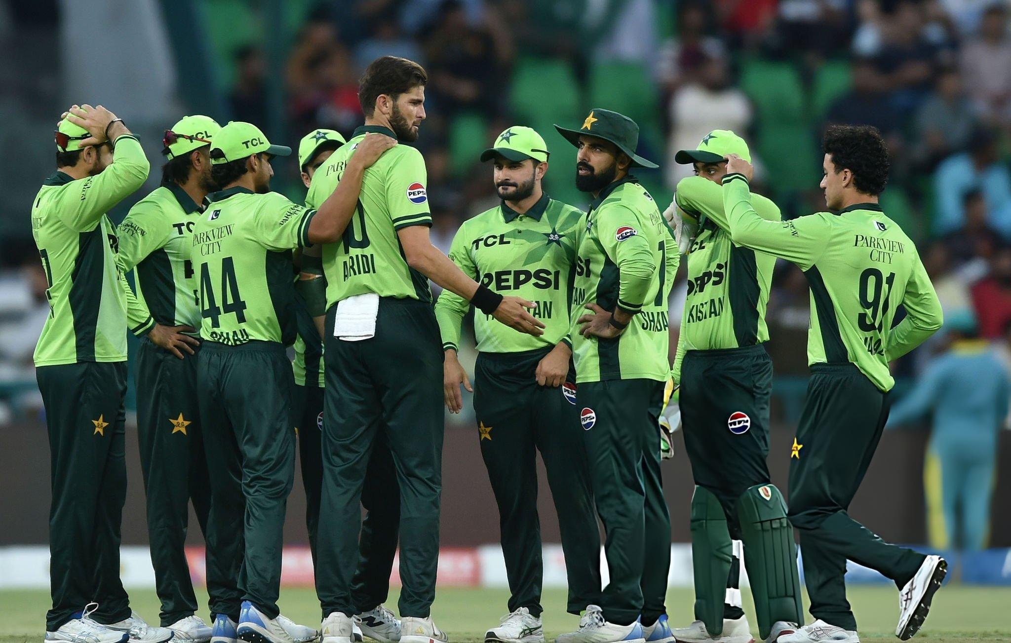Group of Pakistan cricketers in lime‑green jerseys gathered in a huddle on the field
