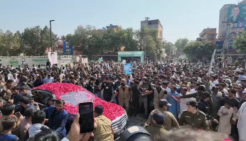 Red car completely covered in red flower petals surrounded by a dense crowd on a street in Mandi Baha‑ud‑Din