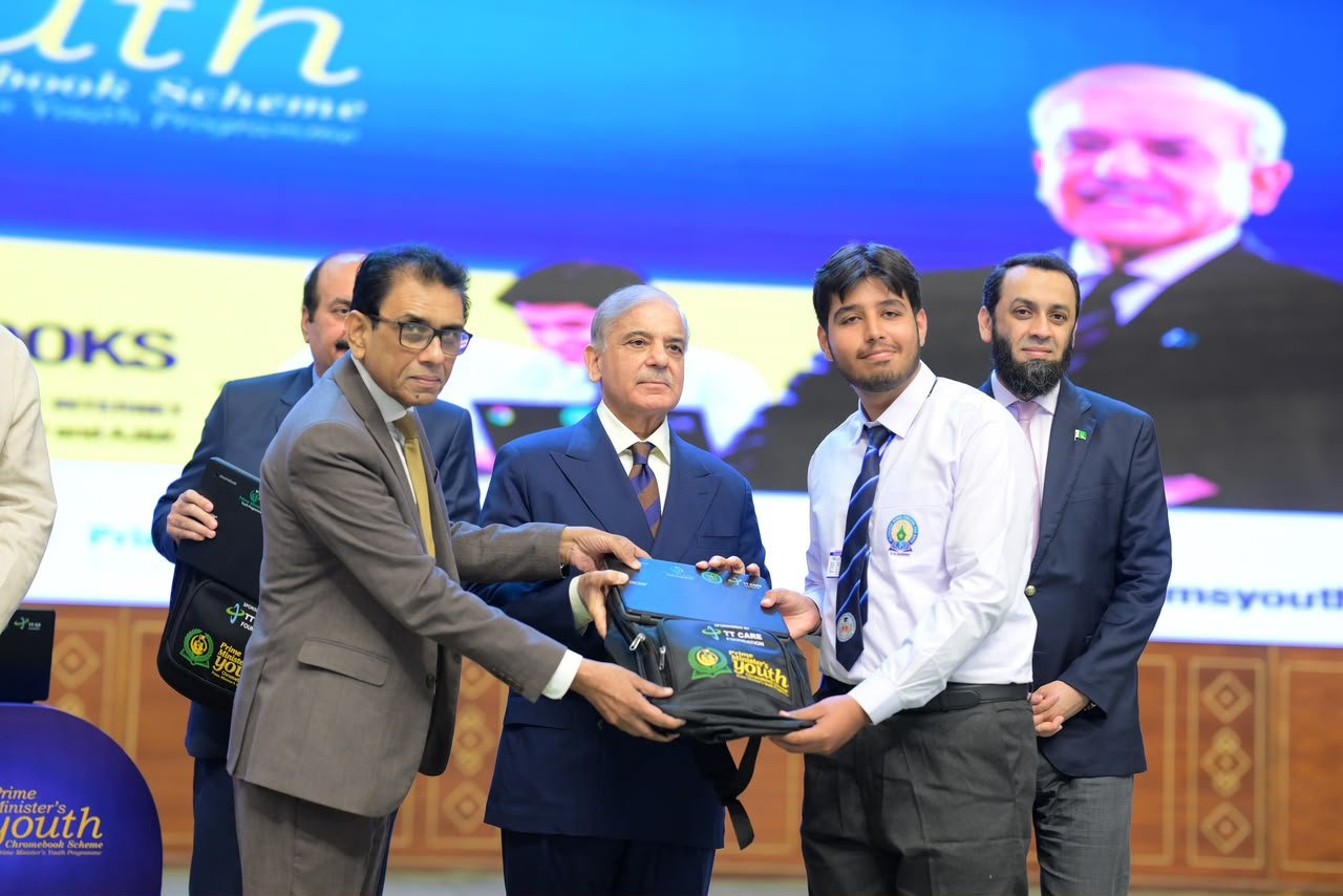 Stage photo of officials handing a black backpack to a young man during the scheme’s launch ceremony