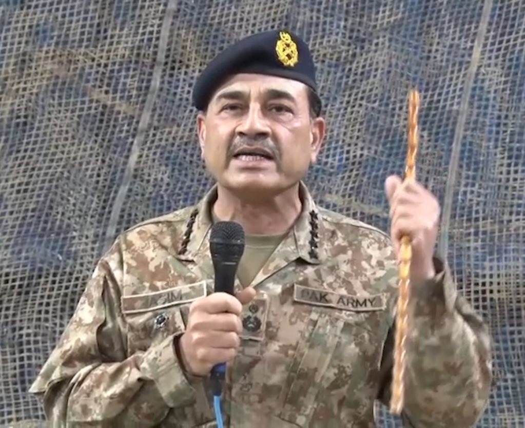 Field Marshal Syed Asim Munir in Pakistan Army camouflage uniform speaking into a microphone while holding a stick