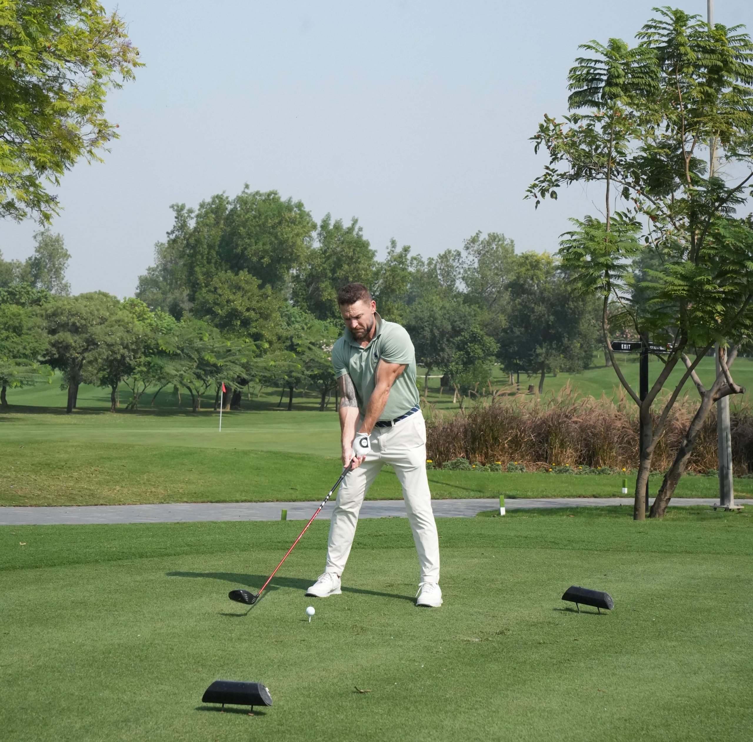 Golf course scene with a green fairway, a red flag on the green and a black sign that reads EXIT in white letters