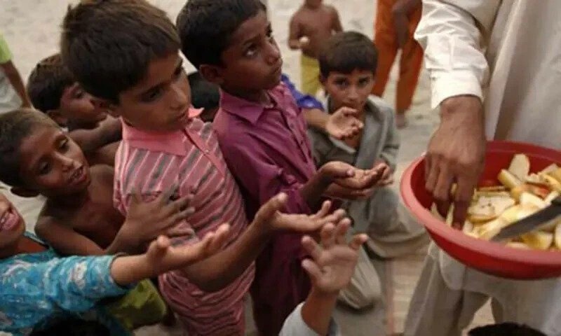 Photograph of young children reaching for a large red bowl of sliced fruit being handed out by an adult