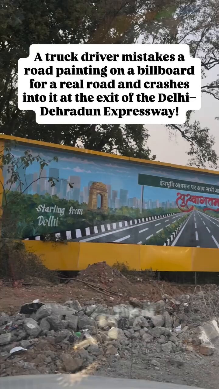 Photograph of a large yellow billboard depicting a realistic highway painting with lane markings, skyline and text, positioned in a construction area with dirt piles in the foreground