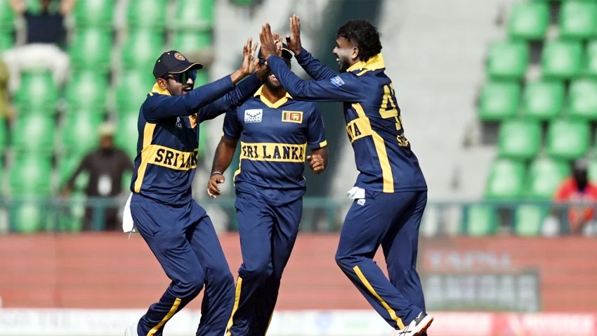 Three Sri Lankan cricketers in navy blue uniforms celebrating on the field with green stadium seats behind them
