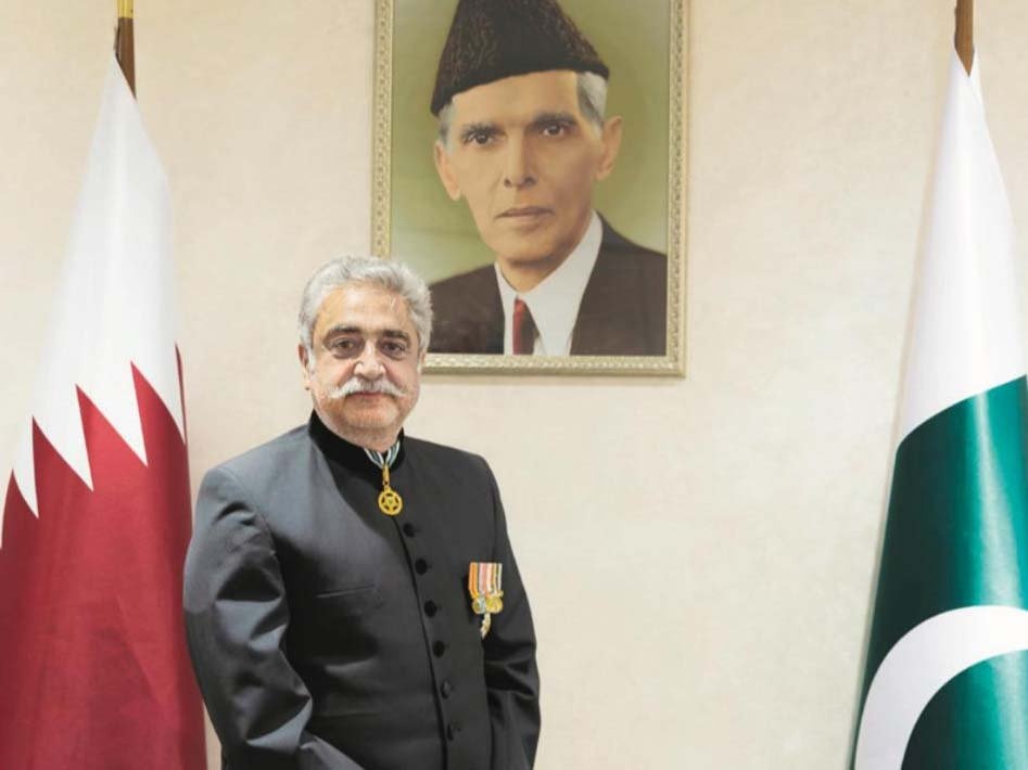 Medium‑shot photograph of Lt Gen (R) Muhammad Aamer in a black sherwani with medals, standing between the flags of Pakistan and Qatar